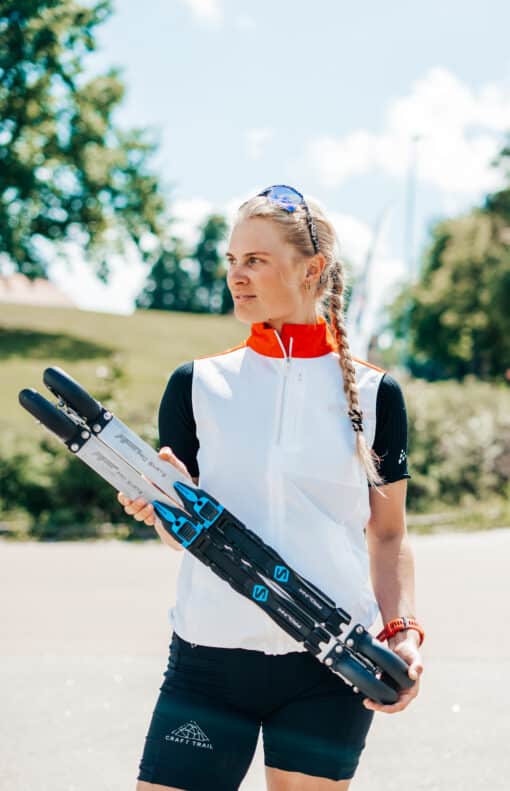 Woman holding a pair of FF rollerskis outdoors.