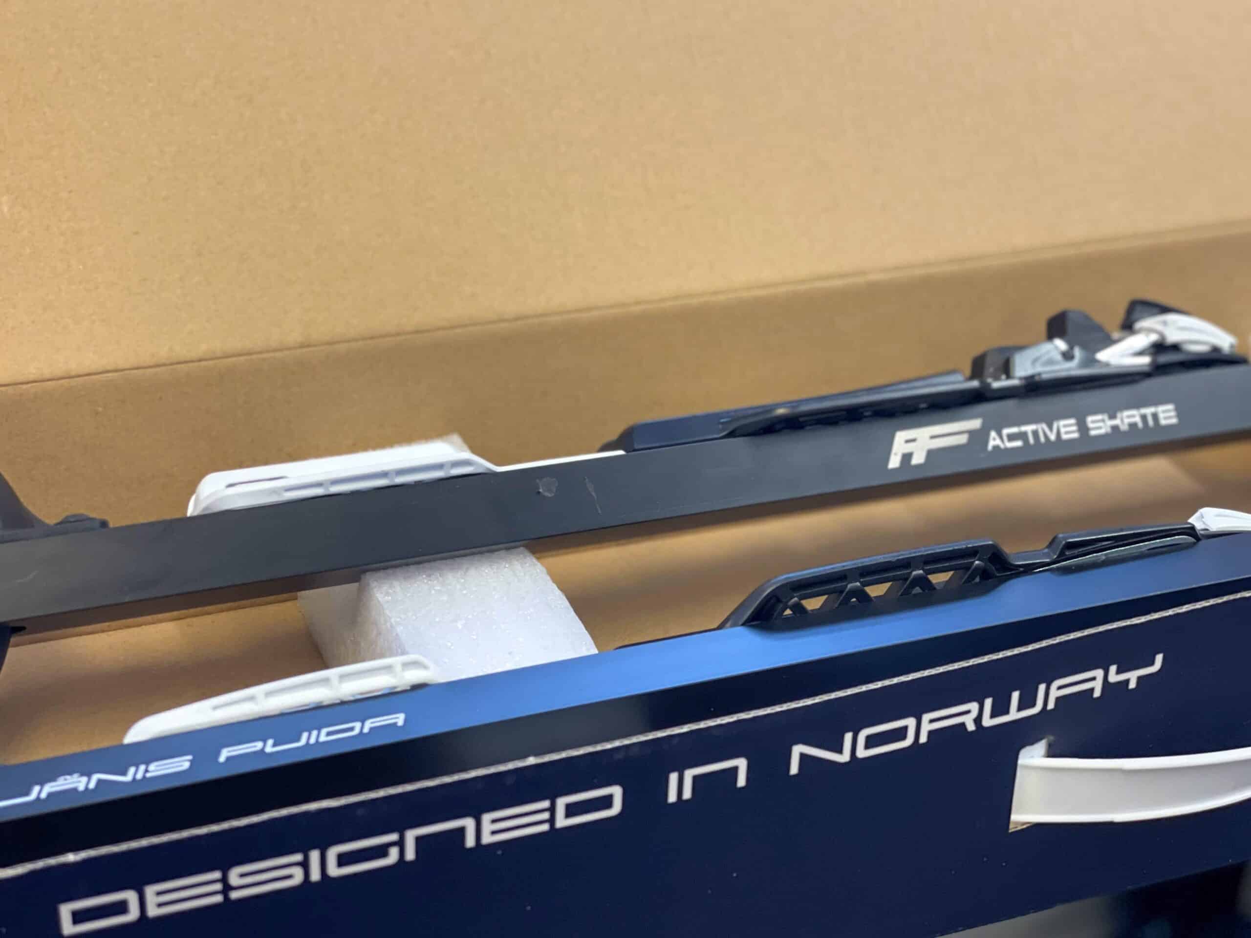 Close-up of new Active Skate cross-country skis in a box, with the text 'Designed in Norway' and the 'FF' logo visible on the side of the skis.